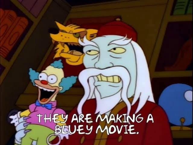 A still from The Simpsons shows a stern, pale-skinned man with a long white beard and red hat, holding a small, laughing…