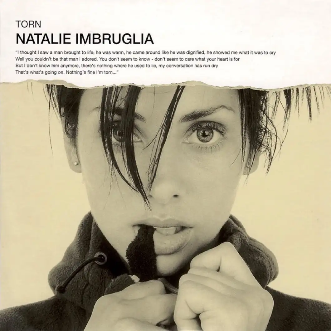 A sepia-toned image of Natalie Imbruglia with wet hair and intense eyes, holding a dark object in her mouth while gripping…