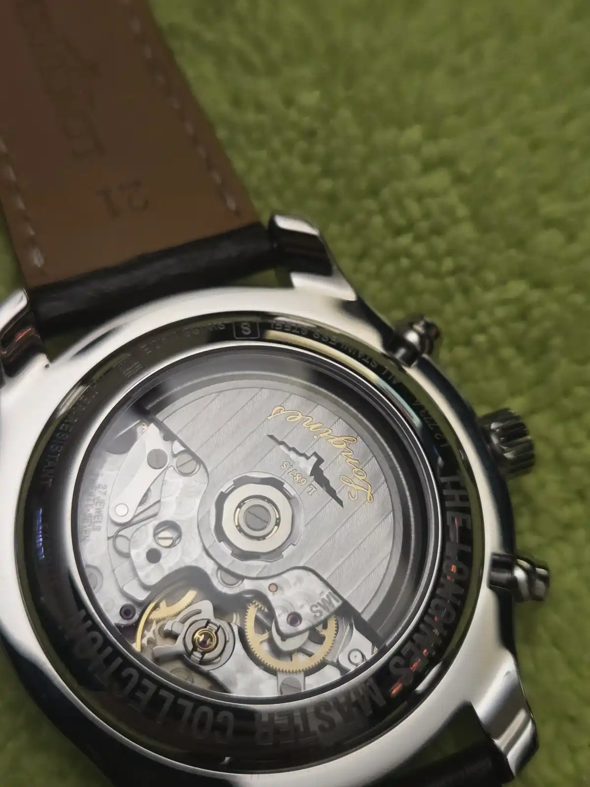 A close-up photo of the back of a Longines Master Collection watch, showing its intricate mechanical movement through a…