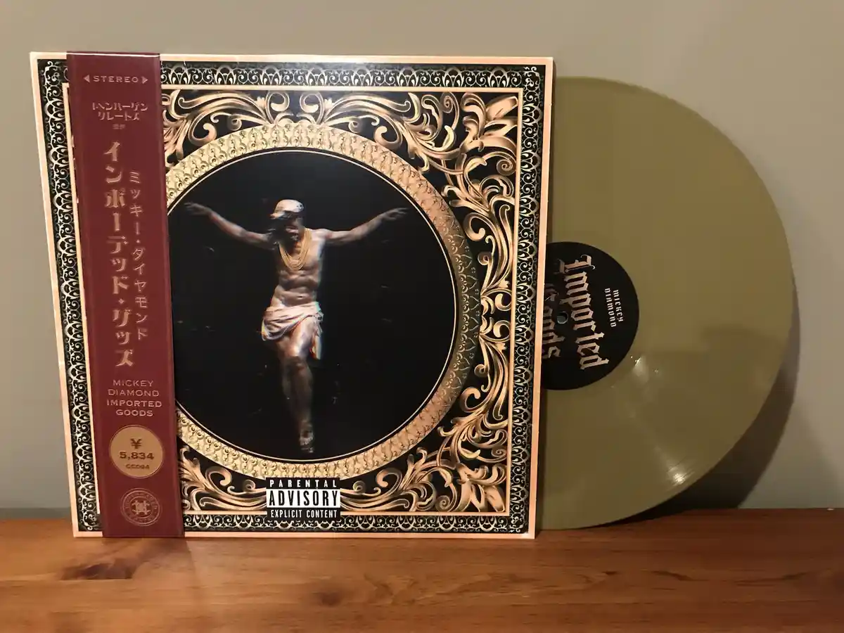 A vinyl record and its album cover for 'Imported Goods' by Mickey Diamond are displayed. The cover art features a man in a…