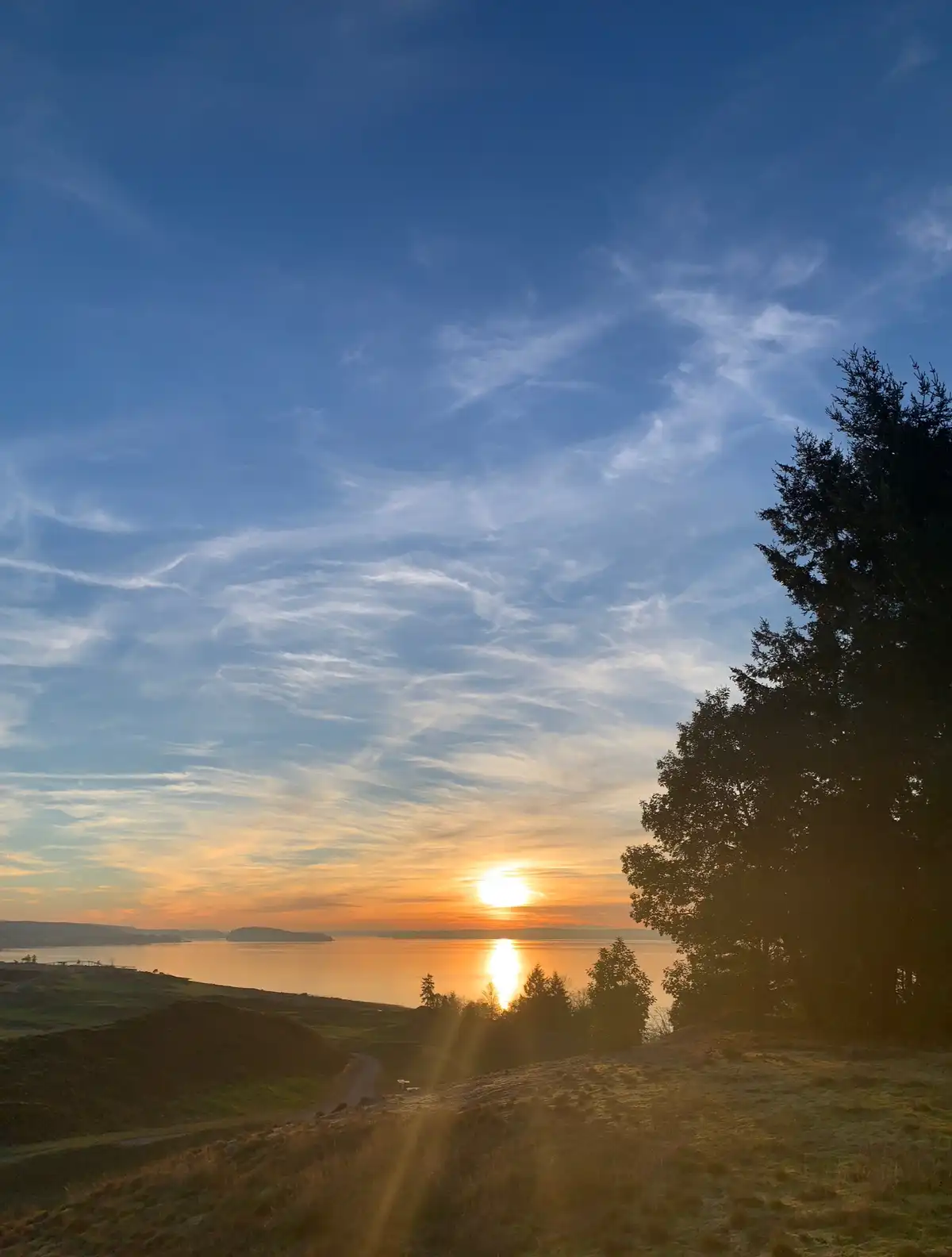 A serene landscape photo of a sunset over a body of water, with the sun low on the horizon casting golden light and…