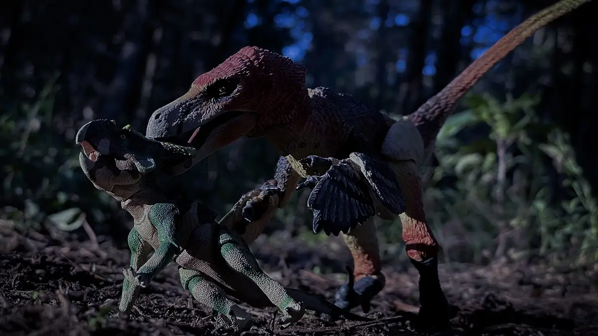 A photo of two dinosaur action figures in a forest setting, one larger red dinosaur with feathered arms is biting the head…