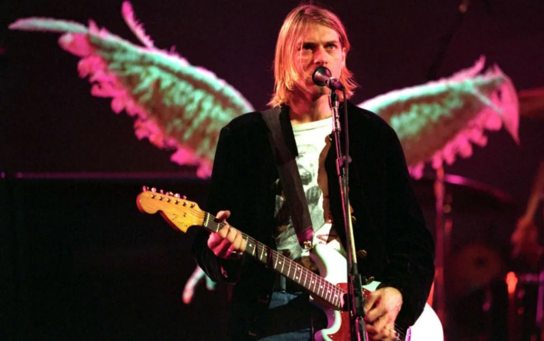 a photo of musician Kurt Cobain performing on stage with a guitar, digitally edited to have large, feathery angel wings…