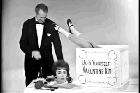 A black-and-white vintage advertisement shows a man in a tuxedo standing beside a woman submerged in a box labeled 'Do It…