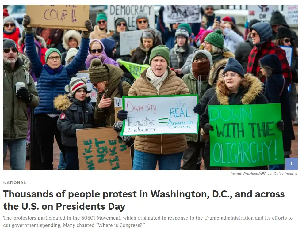 A crowd of protesters in winter clothing holds signs, including one central sign that reads 'Diversity, Equity, Inclusion =…