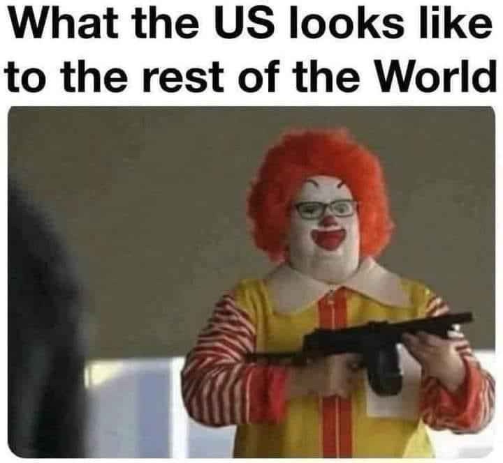 A person wearing a Ronald McDonald costume, complete with red wig, glasses, and yellow-and-red striped outfit, is holding a…