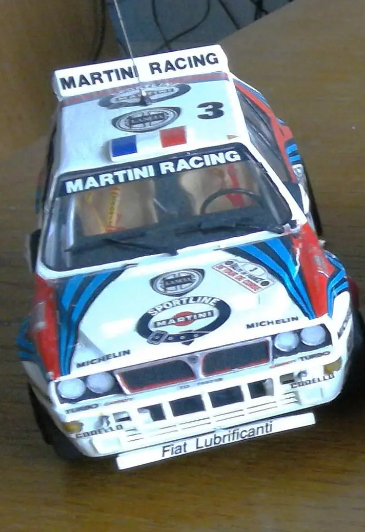 A close-up photo of a white, blue, and red scale model of a vintage rally car, featuring 'MARTINI RACING' branding on the…