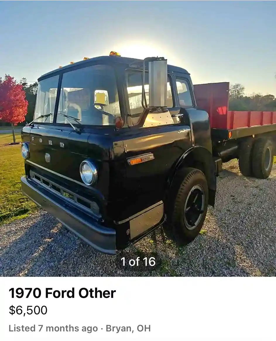 A black 1970 Ford truck with a red flatbed is parked on gravel under a bright sun, with a 'SALE' sign visible in the…