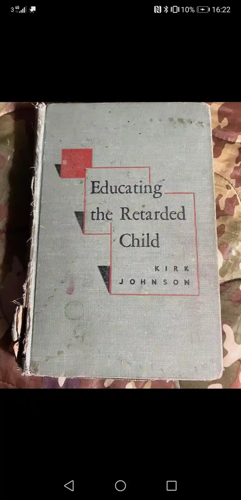 A worn, vintage book with a faded gray cover titled 'Educating the Retarded Child' by Kirk Johnson, resting on a…
