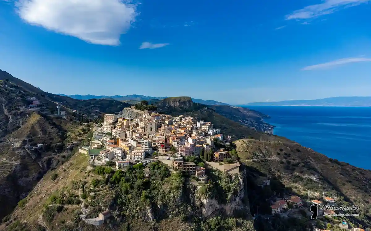 An aerial photo shows a picturesque coastal town built densely on a steep, rocky cliffside overlooking a vast blue sea under…