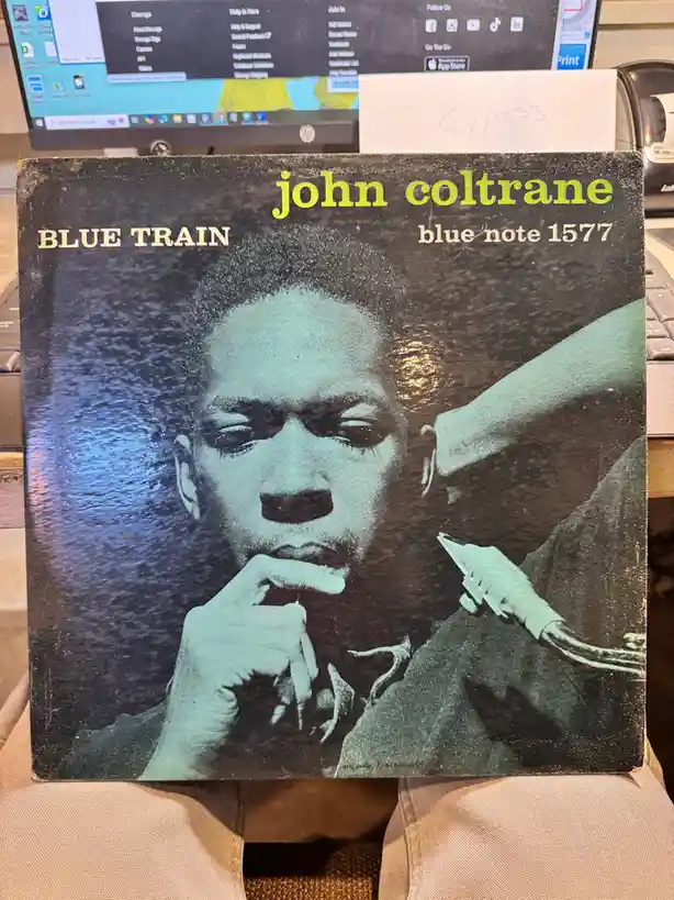 A close-up photo shows a person holding a vintage John Coltrane 'Blue Train' vinyl record album cover, which features a…