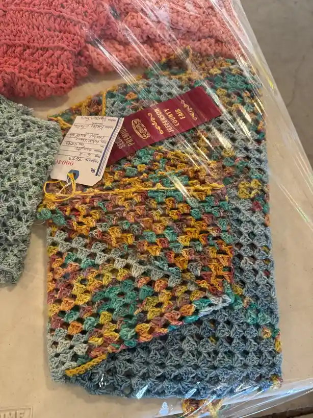 A colorful, multi-toned crocheted textile, likely a washcloth or dishcloth, is wrapped in clear plastic and adorned with a…