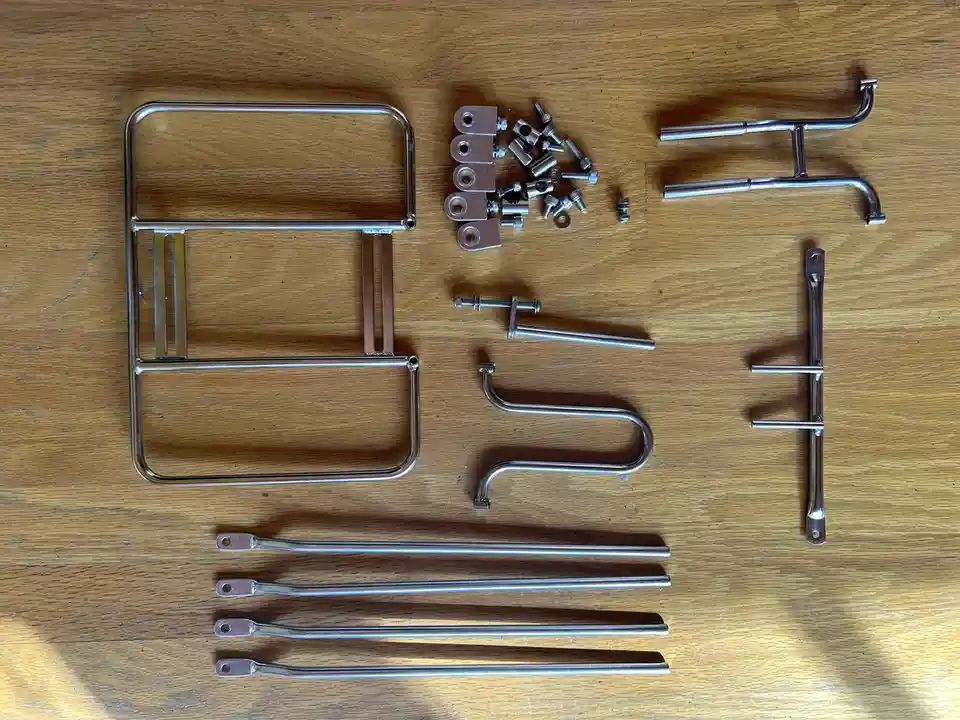 A top-down photo shows various chrome-plated metal parts, including a rectangular frame, curved legs, bolts, and brackets…