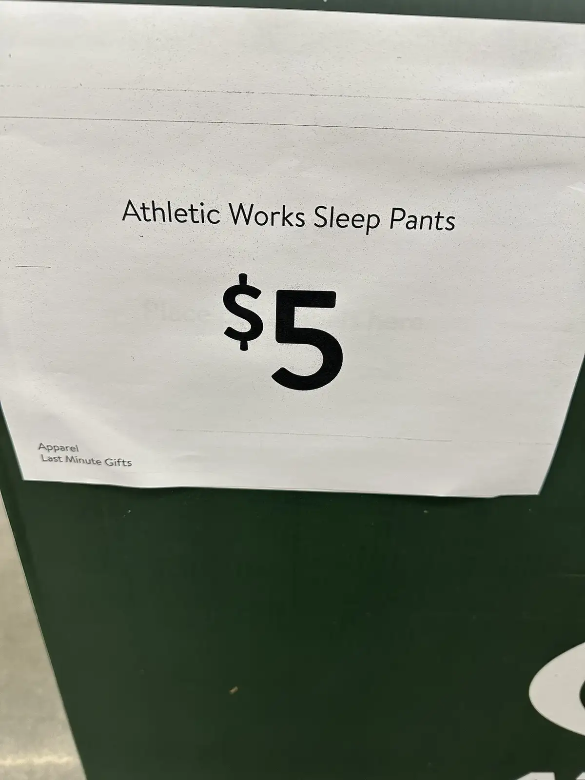 A close-up of a white price tag on a green surface, displaying 'Athletic Works Sleep Pants' and a large '$5' price. Smaller…
