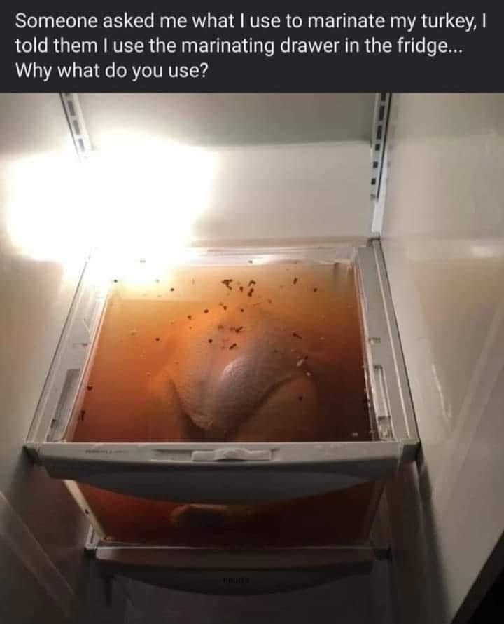 A whole turkey is submerged in a large, amber-colored marinade inside a refrigerator drawer, with spices floating on the…