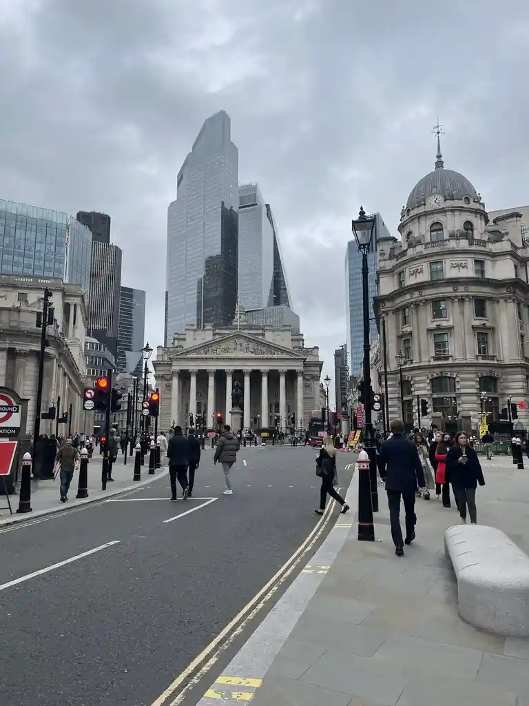 A street-level photo of London's financial district shows pedestrians walking past historic buildings and towering modern…