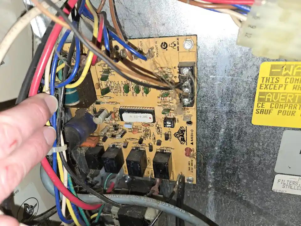 A close-up photo shows a hand holding wires near a dusty, spiderweb-covered circuit board inside an appliance. The board has…