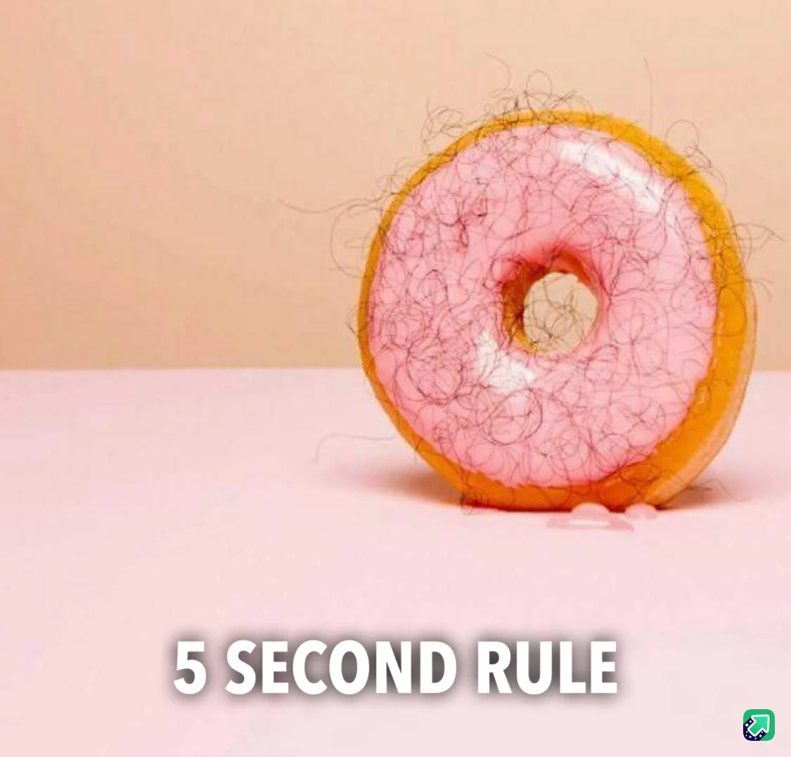 A pink-frosted donut with dark hairs covering its surface sits on a pink surface against a beige background. The overlaid…