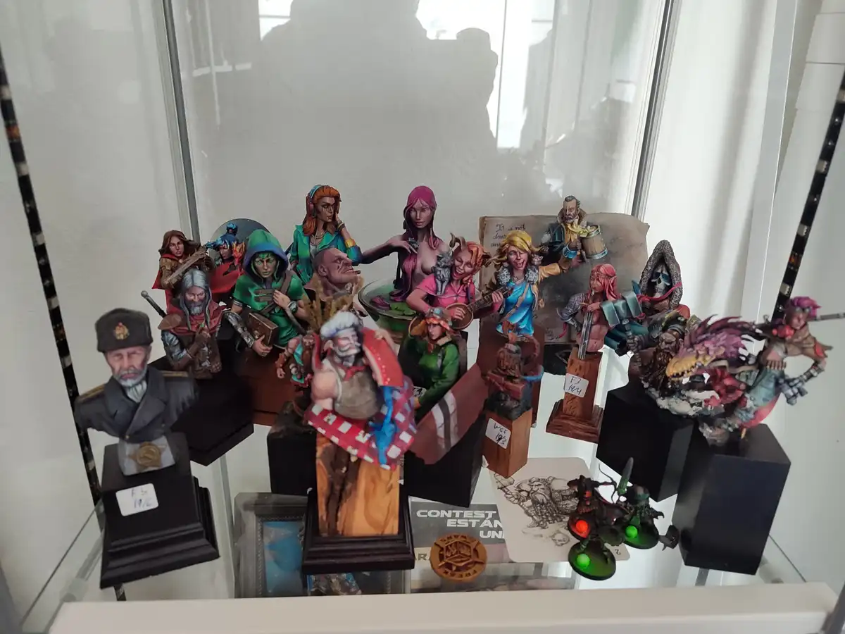 A glass display case holds numerous painted fantasy miniatures and busts, including a prominent bust of a man in a military…