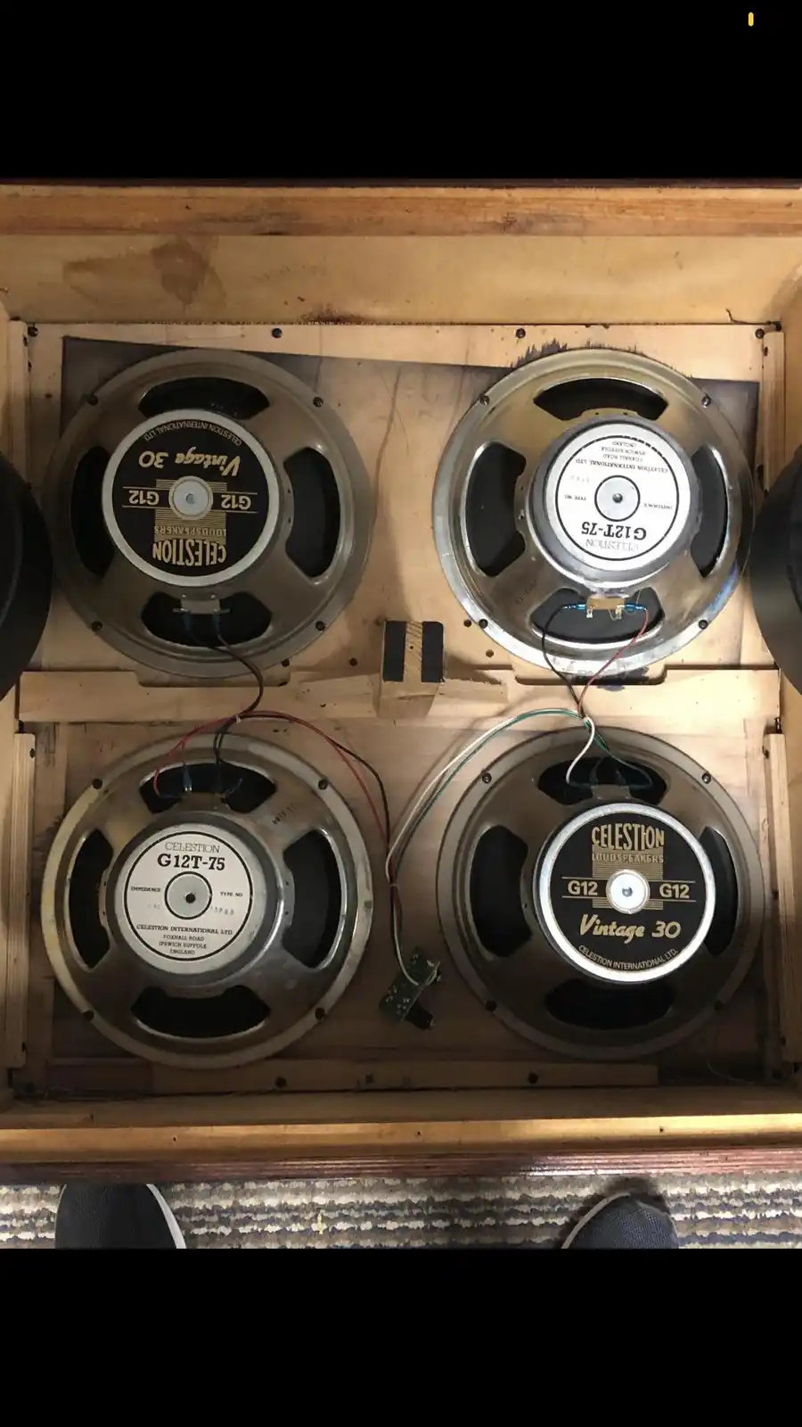 Four vintage Celestion G12 speakers are mounted inside a wooden cabinet, with visible wiring and a small circuit board…
