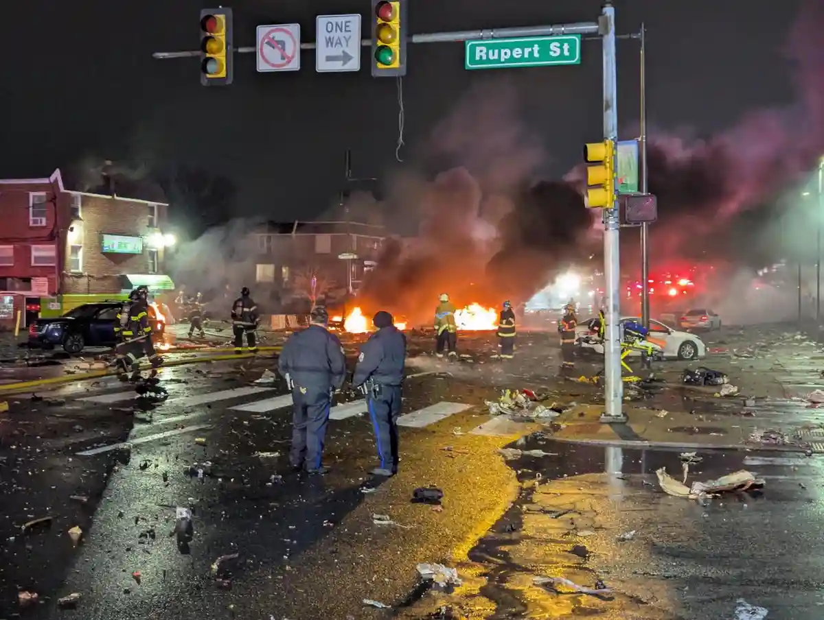 A nighttime street scene at an intersection labeled 'Rupert St' shows a massive explosion with fire and thick smoke…