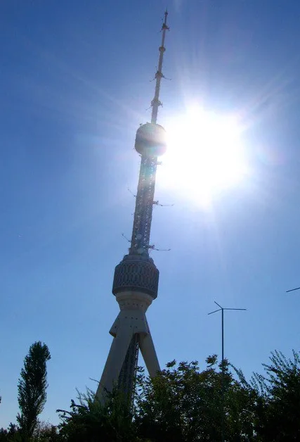 a low-angle photo shows a tall, slender tower with a bulbous middle section and antenna array, silhouetted against a bright…