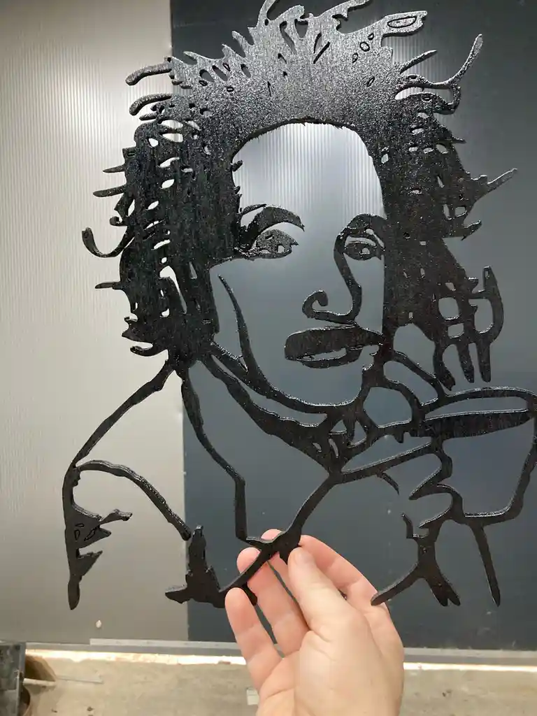 A hand holds up a black, intricately cut silhouette of a man with wild hair and a mustache, resembling Albert Einstein…