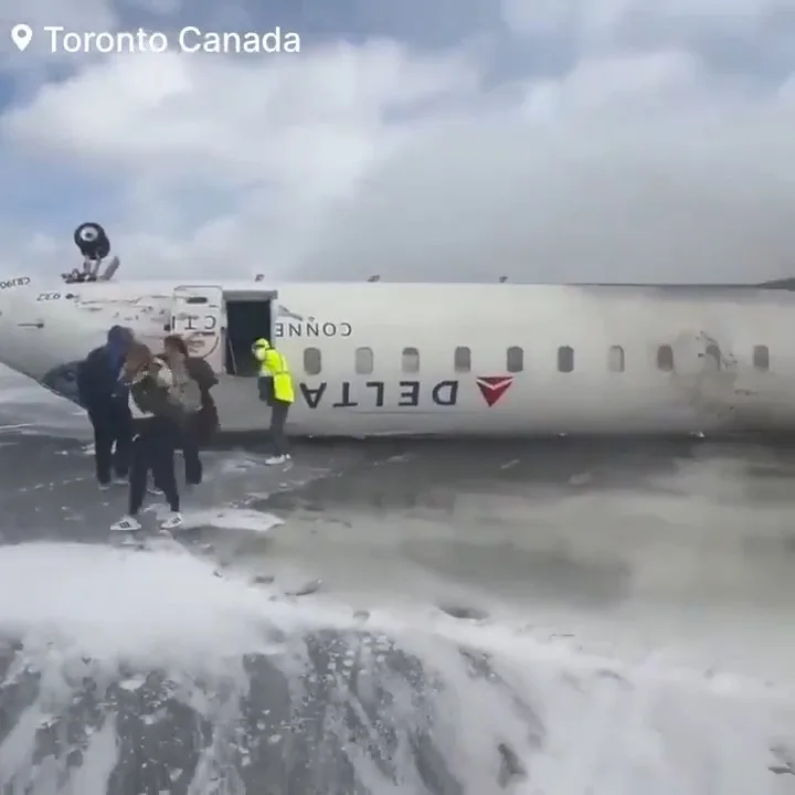 A Delta airplane is shown partially submerged in water, with passengers disembarking through an open door while a ground…