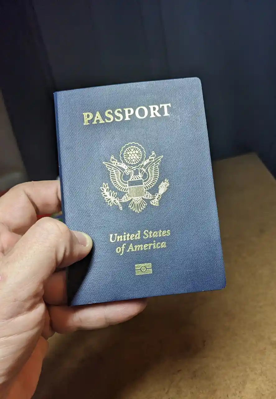 A hand holds a blue United States passport book with gold embossed text and seal. The overlaid text reads 'i'm not a…
