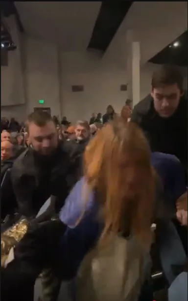A blurry, low-resolution video still shows a woman with long blonde hair in the foreground, seemingly being pulled or…