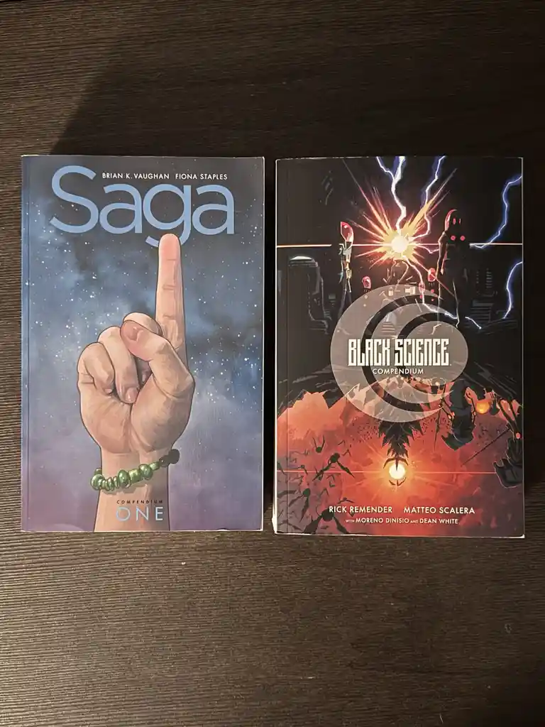 Two comic books, 'Saga Compendium One' with a hand pointing upward against a starry sky and 'Black Science Compendium' with…
