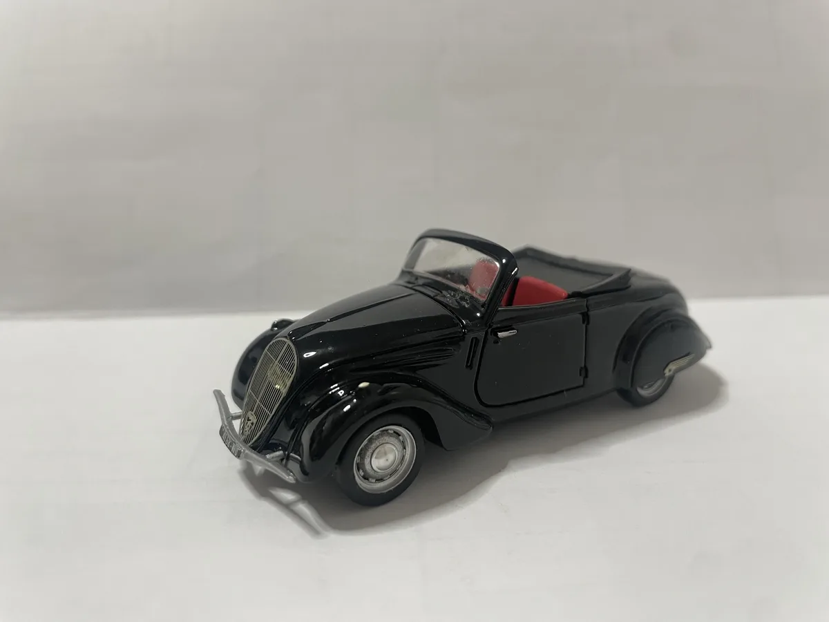 A glossy black die-cast model of a vintage convertible car with red interior seats, photographed on a plain white surface…