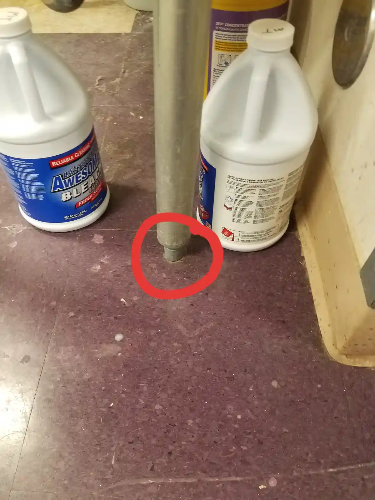 A close-up photo shows a red circle drawn around the base of a metal pole on a purple speckled floor, with two large white…