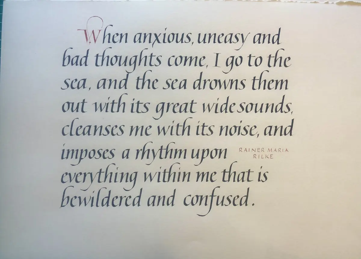 A handwritten quote in elegant calligraphy on cream-colored paper, attributed to Rainer Maria Rilke, describing how the sea…