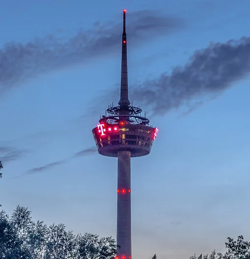 A tall observation tower, likely the Calgary Tower, is lit up with red lights against a twilight sky with scattered clouds…