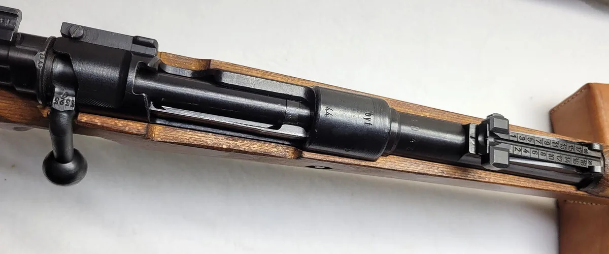 A close-up photo of a vintage bolt-action rifle with a wooden stock and metal barrel, showing engraved markings and a serial…