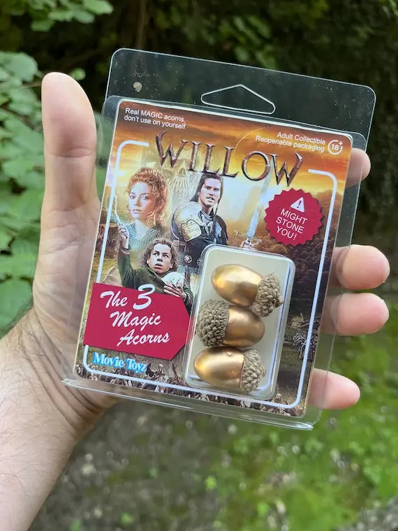 A hand holds a plastic blister pack of 'Willow' movie merchandise featuring three golden acorns labeled 'The 3 Magic…