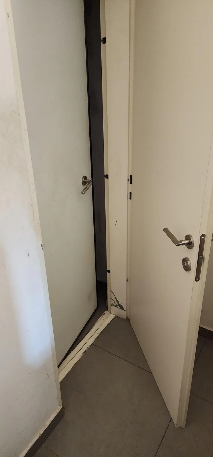 Two white doors are slightly ajar, forming a narrow V-shaped gap between them, revealing a dark space behind. The doors have…
