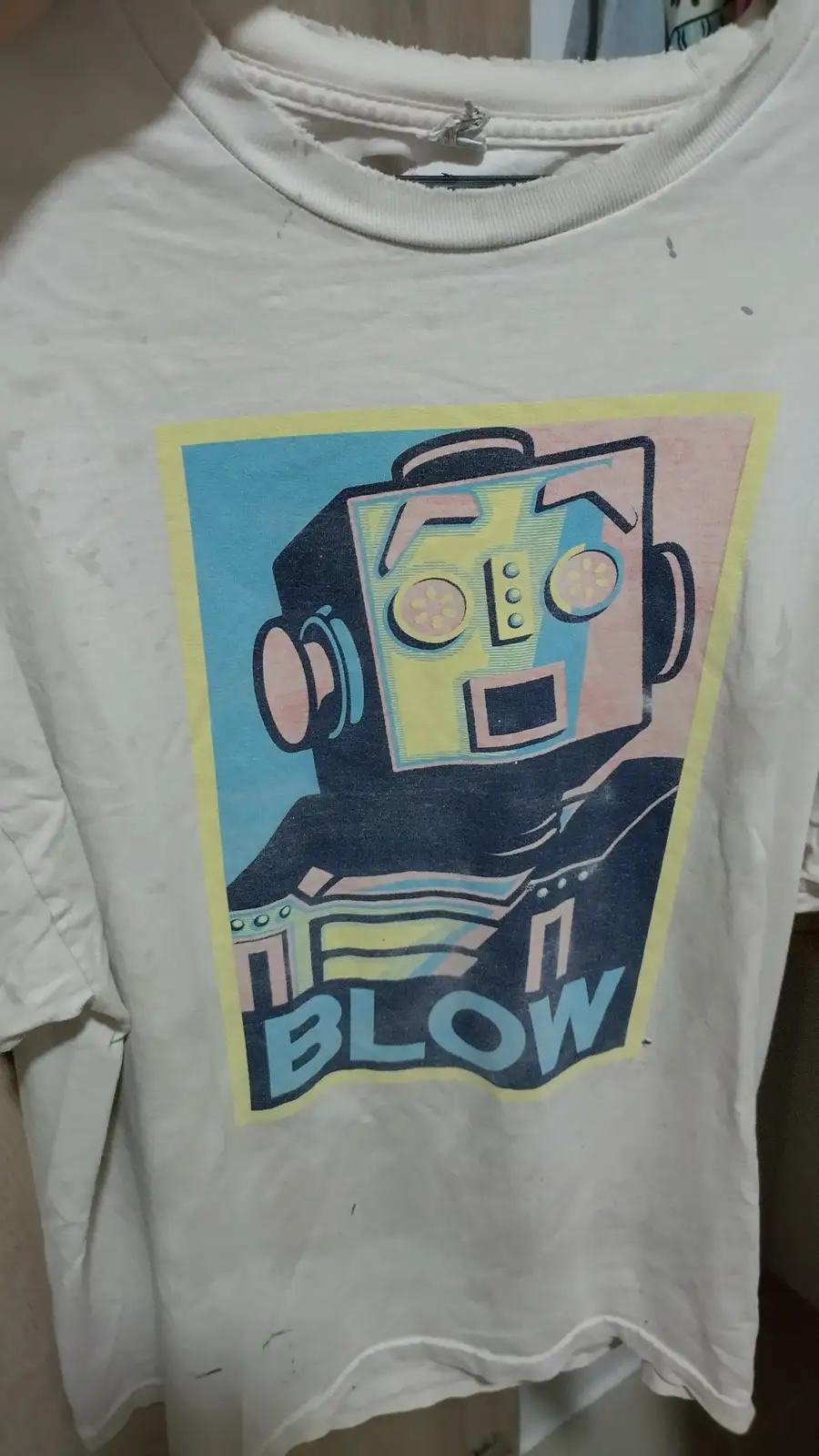 A white, worn t-shirt features a stylized graphic of a retro robot with a square head, circular eyes, and a surprised…