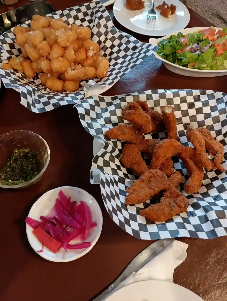 A table is covered with fried food including tater tots and fried calamari in black-and-white checkered paper baskets…