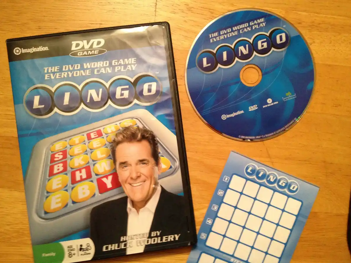 A photo shows the DVD game 'Lingo' with its case, disc, and a blank game card on a wooden surface. The case features a…