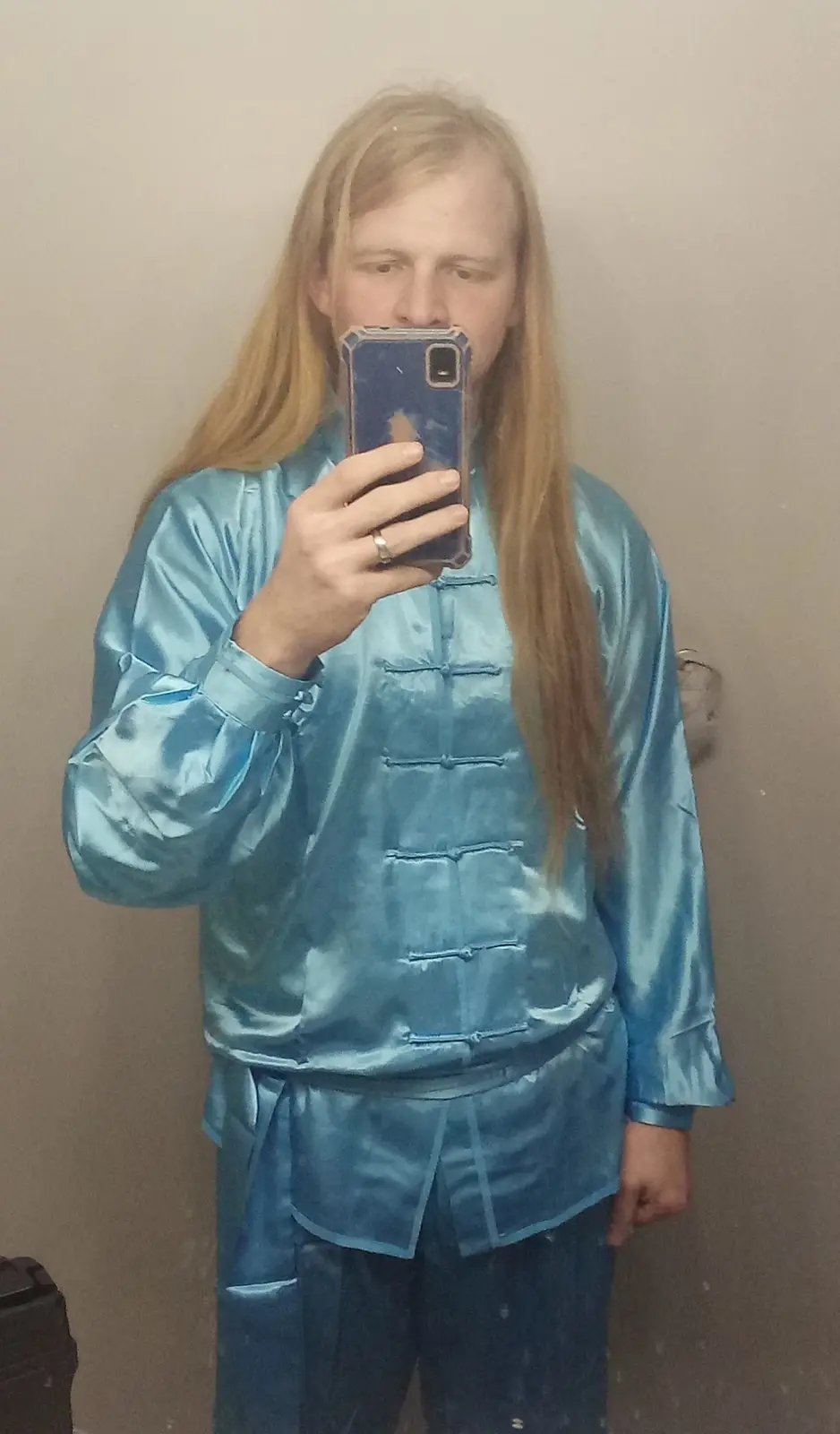 A person with long blonde hair takes a mirror selfie holding a phone, wearing a shiny blue traditional Chinese-style outfit…