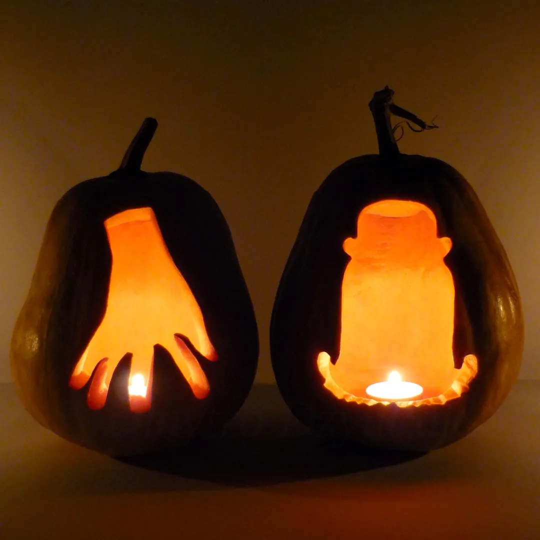 Two carved pumpkins sit side by side, each illuminated from within by a small candle. The pumpkin on the left has a…