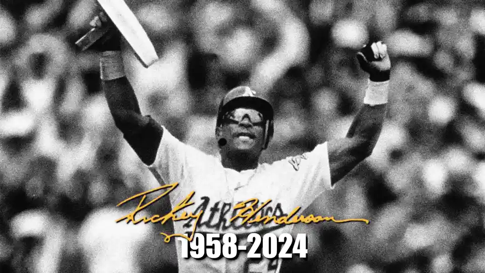 A black-and-white photo of baseball player Rickey Henderson celebrating with arms raised, holding a bat, wearing an Oakland…