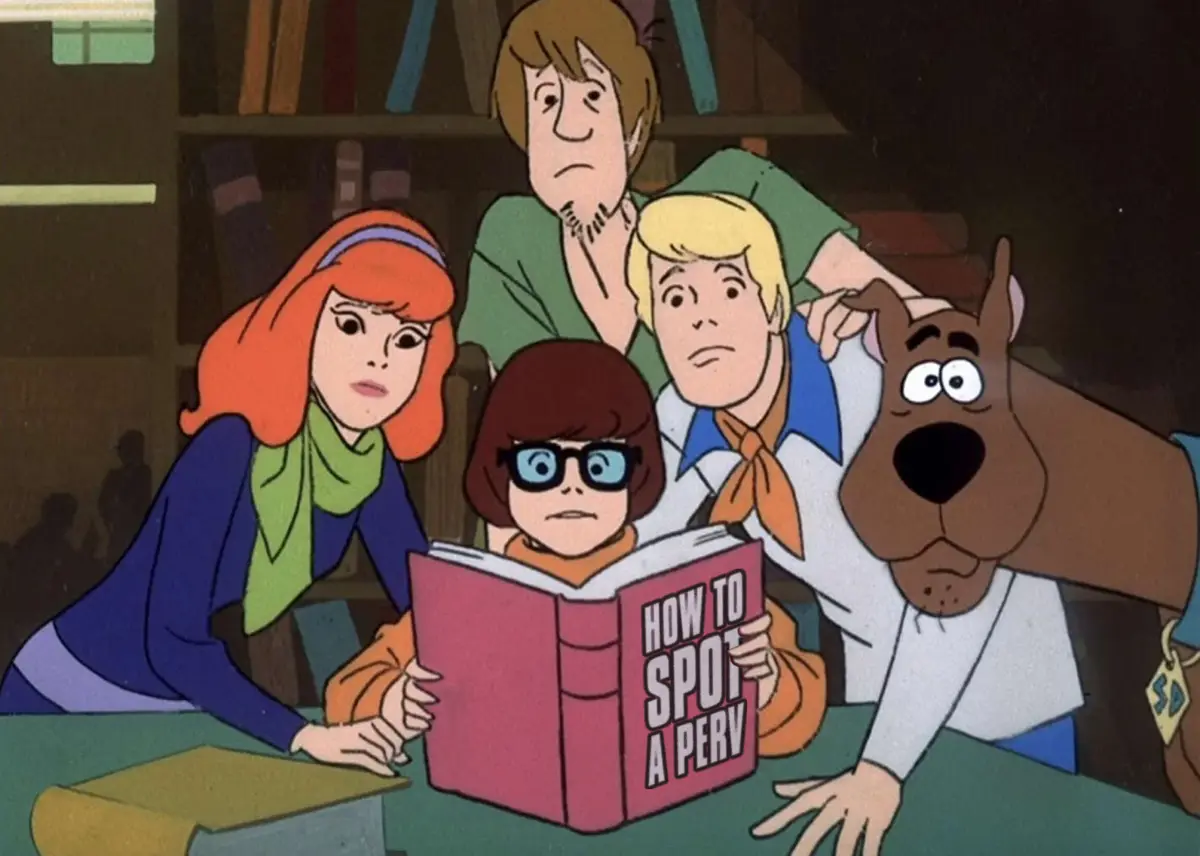 The Scooby-Doo gang—Shaggy, Velma, Daphne, Fred, and Scooby—are gathered around a table in a library, looking concerned as…