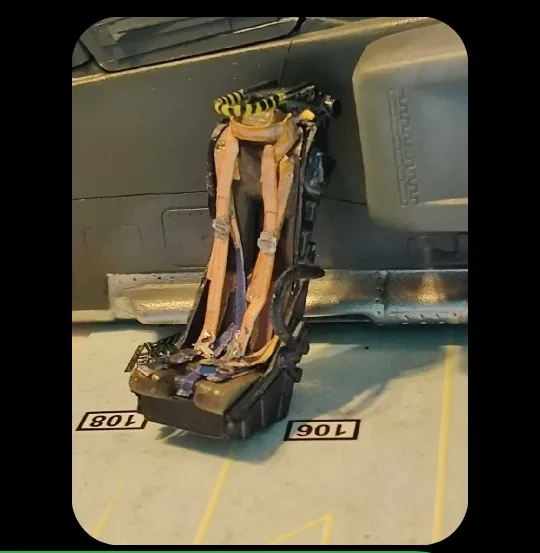 A close-up photo shows a damaged, worn-out aircraft ejection seat with frayed straps and exposed internal components…