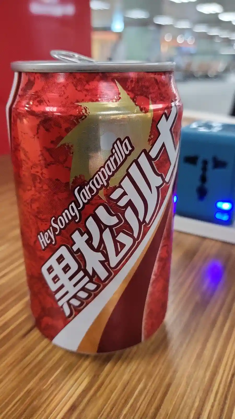 A red aluminum soda can with a gold star and large white Chinese characters sits on a wooden surface. The can is labeled…