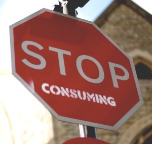 A red octagonal stop sign with white lettering that reads 'STOP' at the top and 'CONSUMING' below it, mounted on a metal…