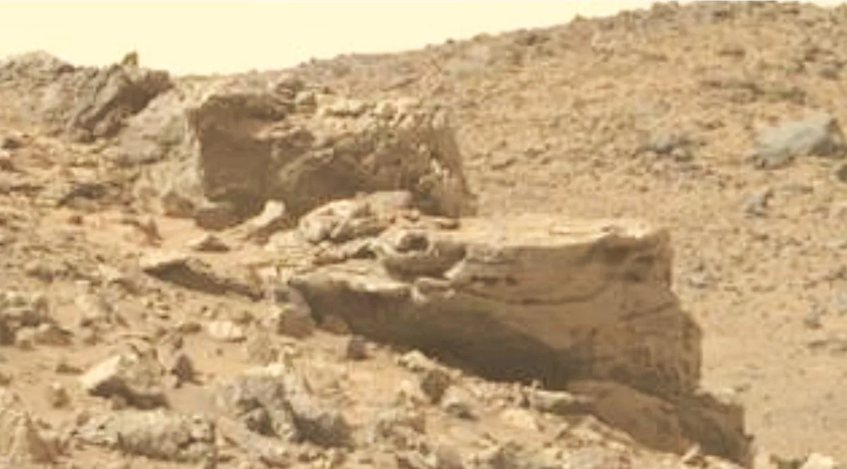 a blurry, reddish-brown landscape of rocky terrain on mars, featuring a large, flat-topped rock formation in the foreground…