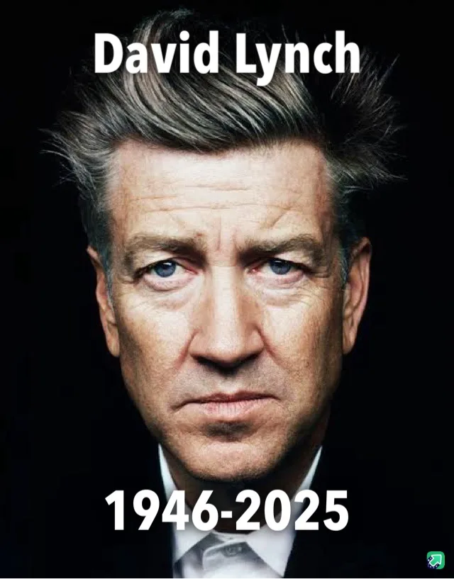 A close-up portrait of a man with graying hair and intense blue eyes, wearing a dark suit and white shirt against a black…